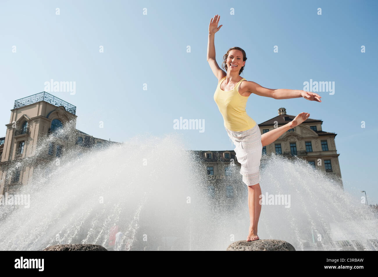 Deutschland, München, Karlsplatz, junge Frau, die auf Felsen am Brunnen Stockfoto
