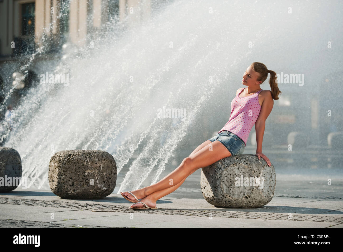 Deutschland, München, Karlsplatz, junge Frau am Brunnen sitzen Stockfoto