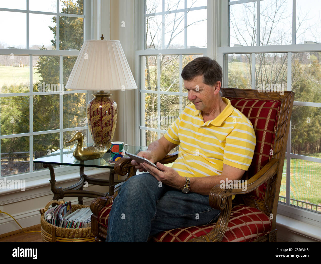 Senior Mann sitzt zu Hause lesen auf seinem iPad Stockfoto