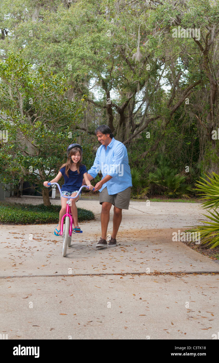 Hispanische Vater Tochter im Laufwerk zu Hause helfen Betroffenen lernen, Fahrrad und Sicherheit sprechen zu reiten Stockfoto Hispanische Vater Tochter im Laufwerk zu Hause helfen Betroffenen lernen, Fahrrad und Sicherheit sprechen zu reiten Stockfoto