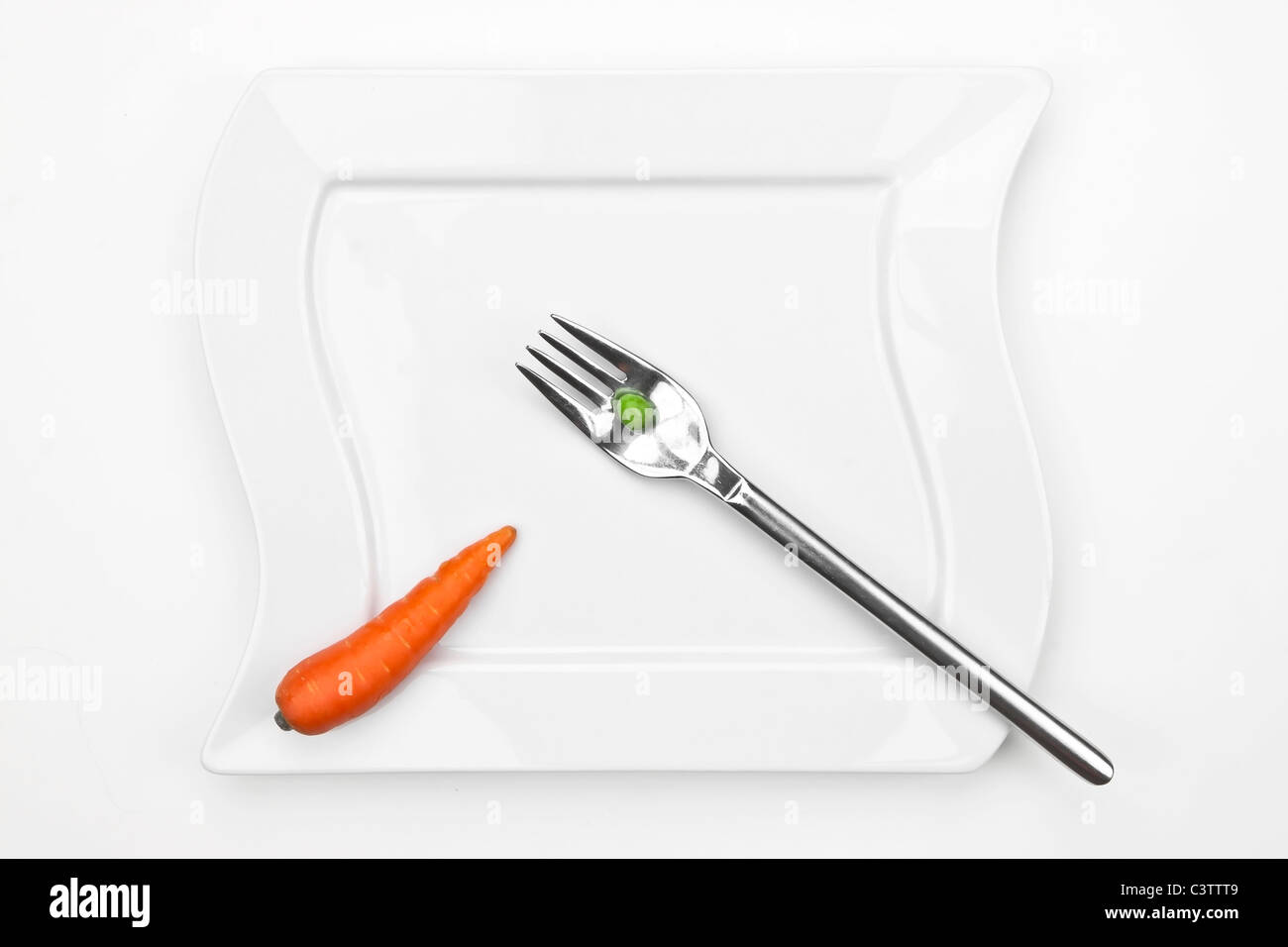 eine Karotte und eine Erbse auf eine Gabel mit einem weißen Teller Stockfoto