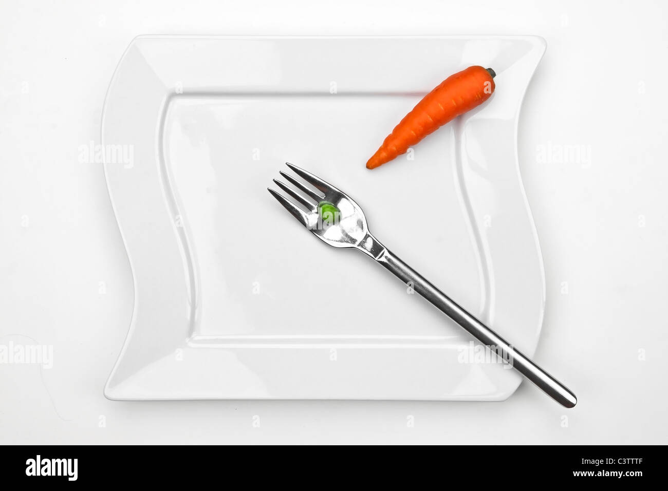 eine Karotte und eine Erbse auf eine Gabel mit einem weißen Teller Stockfoto