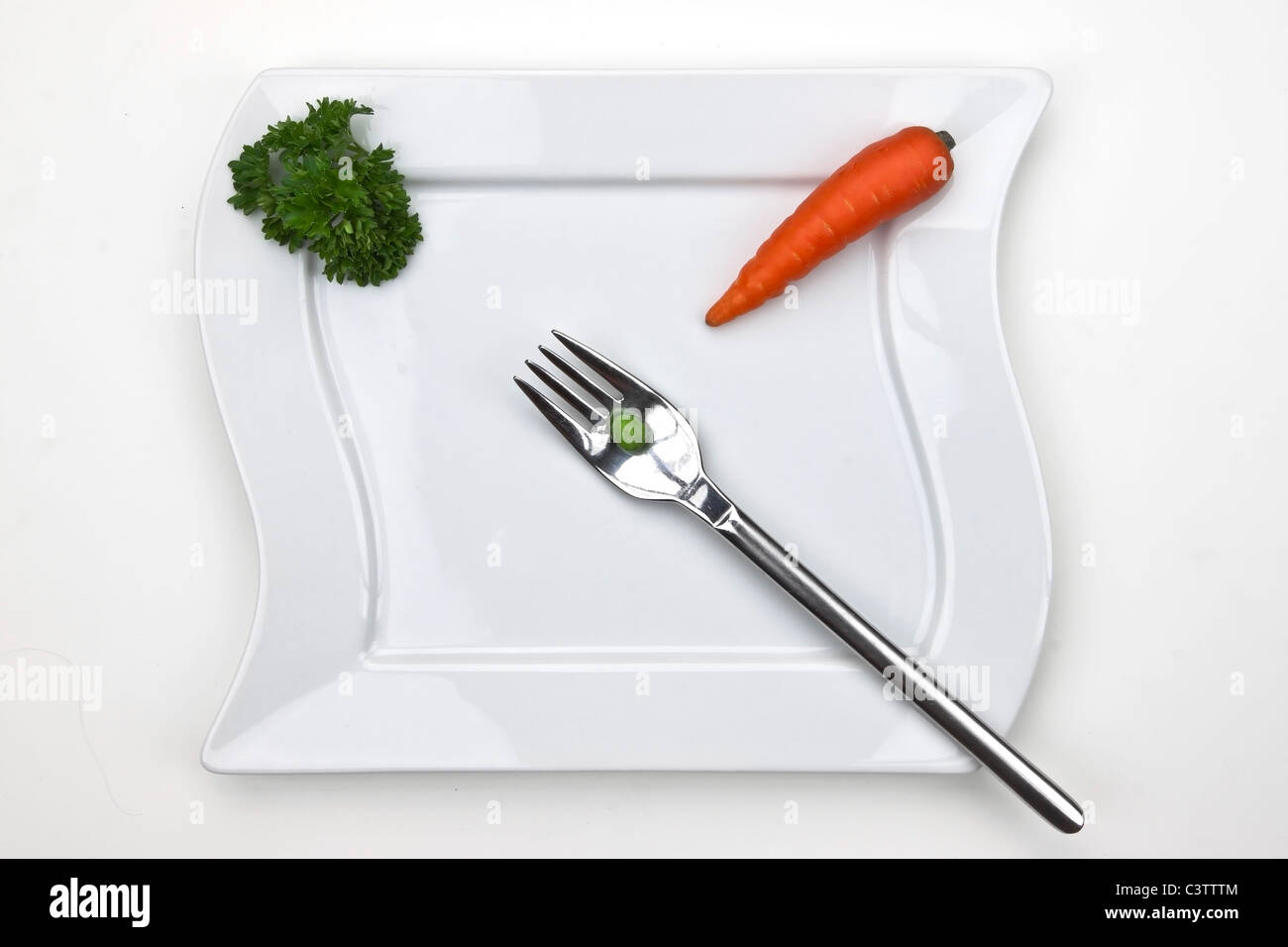 eine Karotte und eine Erbse auf eine Gabel mit einem weißen Teller, dekoriert mit Petersilie Stockfoto