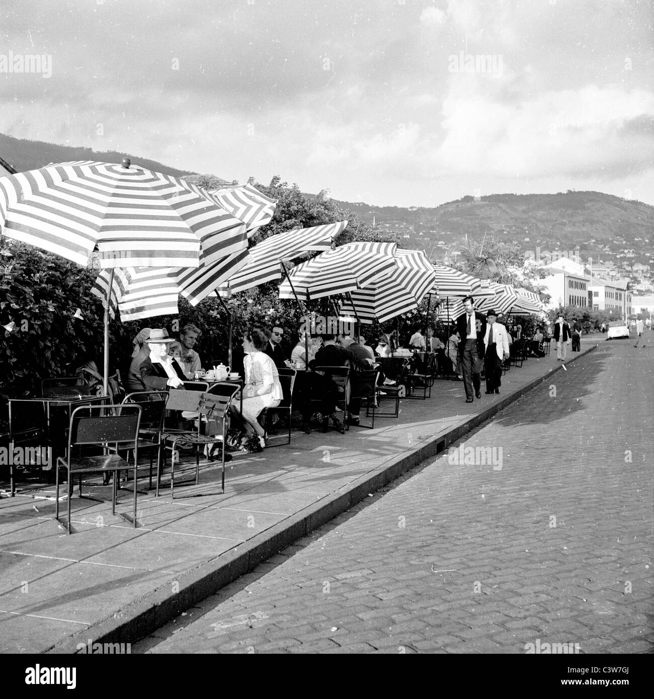 Historische Aufnahme der 1950er Jahre von J. Allan Cash. Menschen entspannen am Straßenrand Tabellen in Funchal, Madeira. Stockfoto