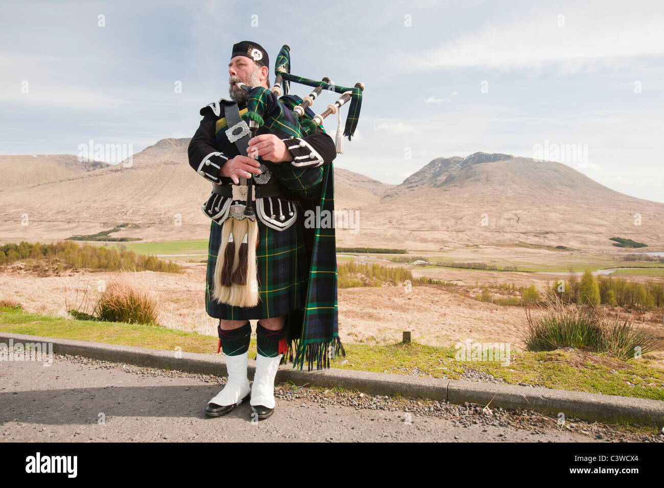Eine schottische Piper in traditioneller Tracht als Straßenmusikant auf Rannoch Moor in Argyl, Scotland, UK. Stockfoto