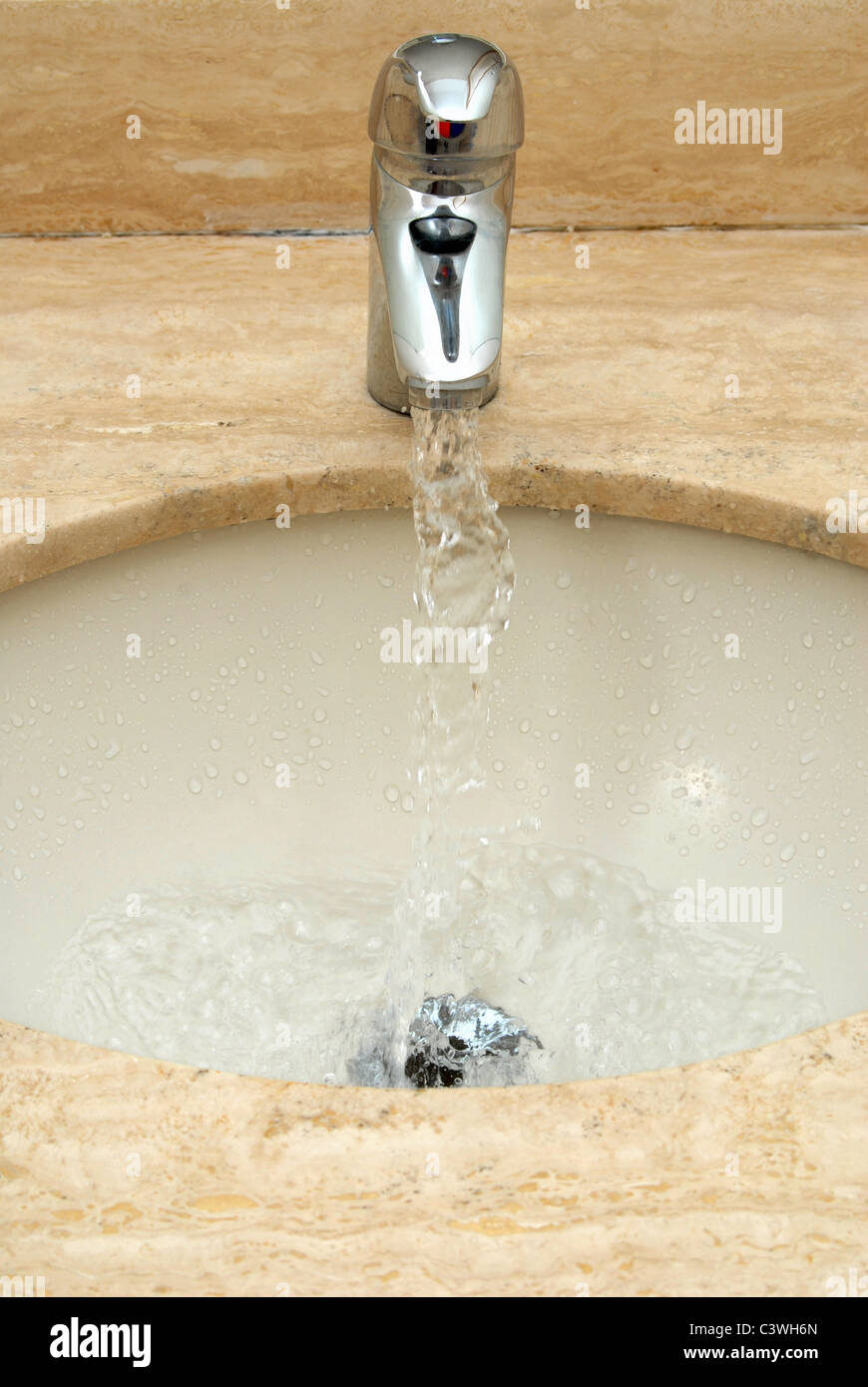 Wasser aus einem Hahn fallen in einem weißen Marmor Waschbecken Stockfoto
