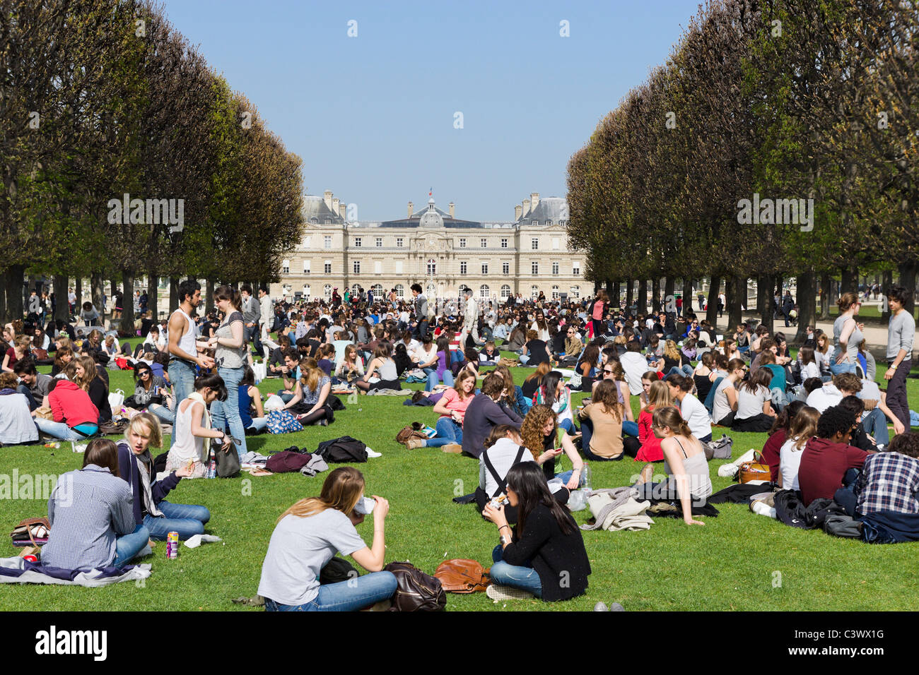 Schüler mit Mittagessen auf dem Rasen vor dem Palais du Luxembourg im frühen Frühlingssonnenschein, Jardin du Luxembourg, Paris, Frankreich Stockfoto