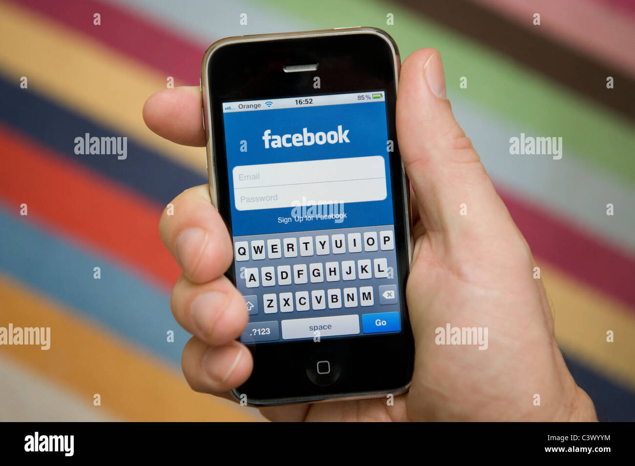 Nahaufnahme von männliche Hand, die ein iPhone dabei, sich bei Facebook anmelden. (Nur zur redaktionellen Verwendung). Stockfoto