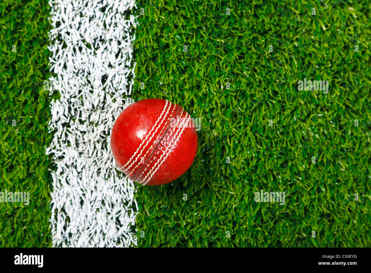 Foto von ein Cricketball auf einer Wiese neben der weißen Linie, von oben geschossen. Stockfoto