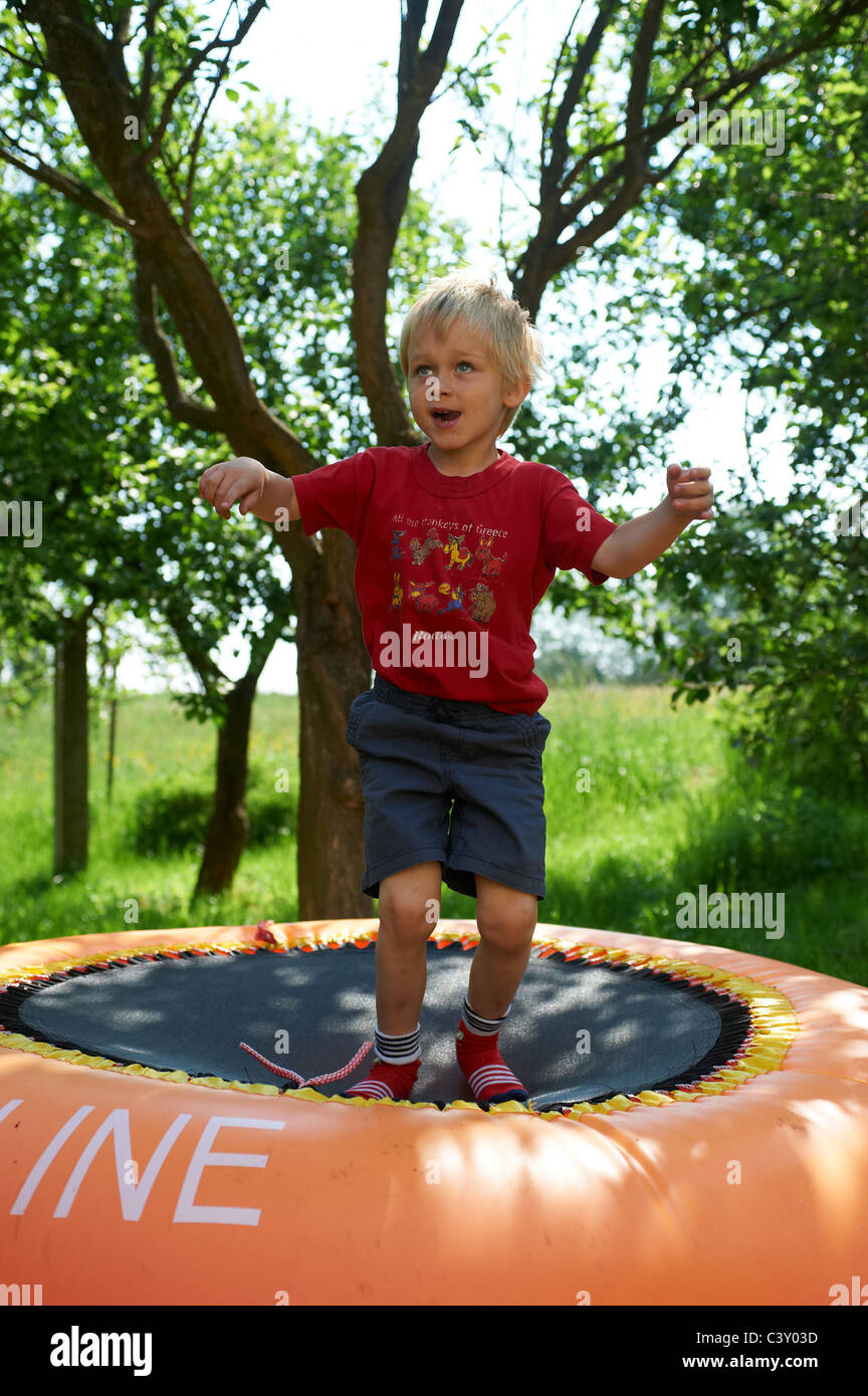 Glücklich blondes Kind junge springen und spielen auf orange Trampolin im Garten Sommer Stockfoto