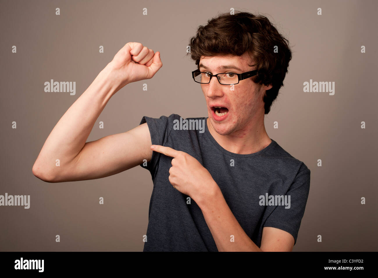 eine fleckige konfrontiert schwach schwach Geek Nerd junger Mann mit dünnen Arme, die das Tragen einer Brille, die seine Muskeln UK Stockfoto