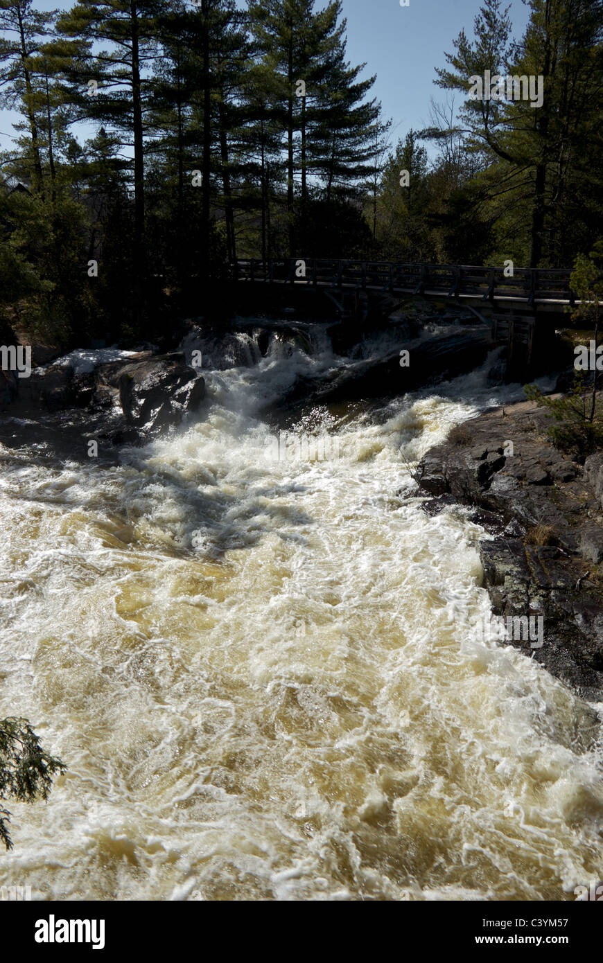 Wütende Rivière-du-Loup im vollen Frühjahr Hochwasser in Motion blur Kaskadierung über kleinen Wasserfall unter Promenade Brücke Stockfoto