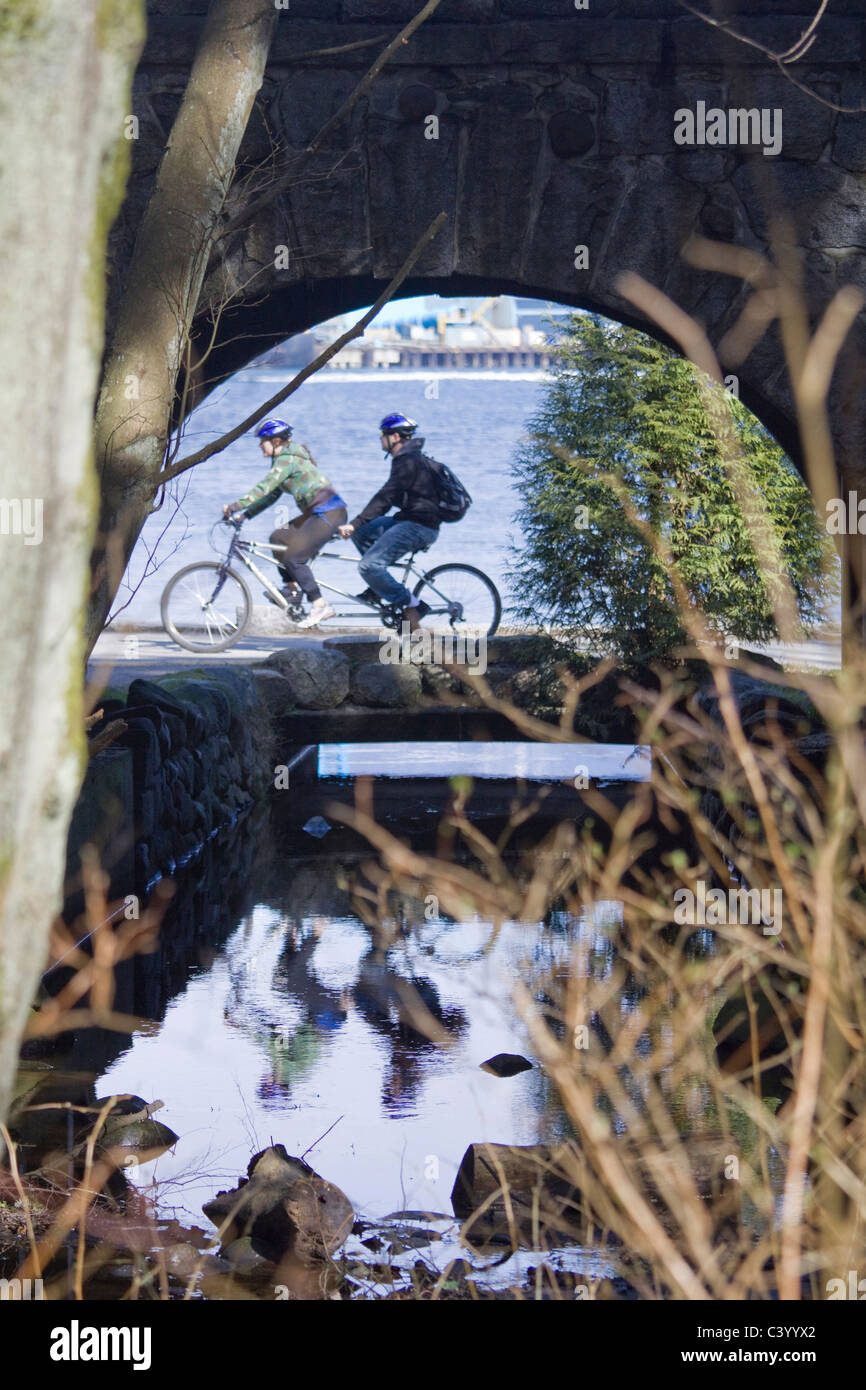 Paar auf Tandem entlang der Ufermauer, wie durch Tunnel zu sehen. Stanley Park, Vancouver BC, Kanada Stockfoto