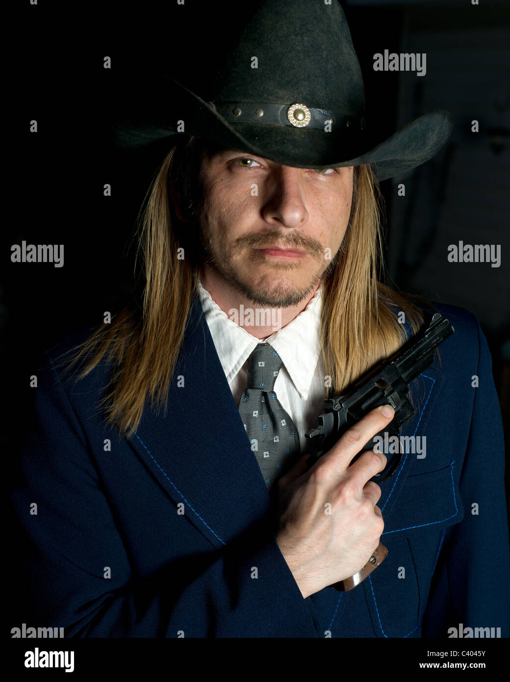 Ein langhaariger Mann in Cowboy-Hut hält einen Revolver. Stockfoto
