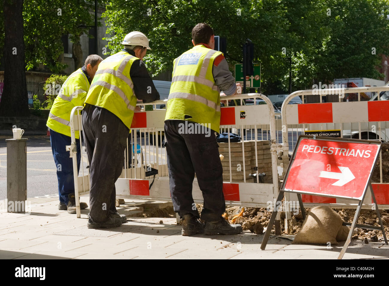 London Kings Cross, britische Arbeiter in Sicherheit Jacken Uhr Graben Mannloch auf Euston Road Bürgersteig mit Tee Tassen auf post Stockfoto