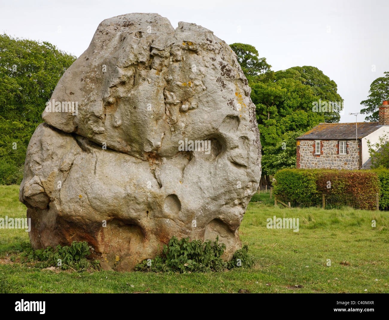 Massive Sarsen Monolith in eines der inneren Steinkreise von Avebury in Wiltshire mit einem Haus im Dorf jenseits Stockfoto