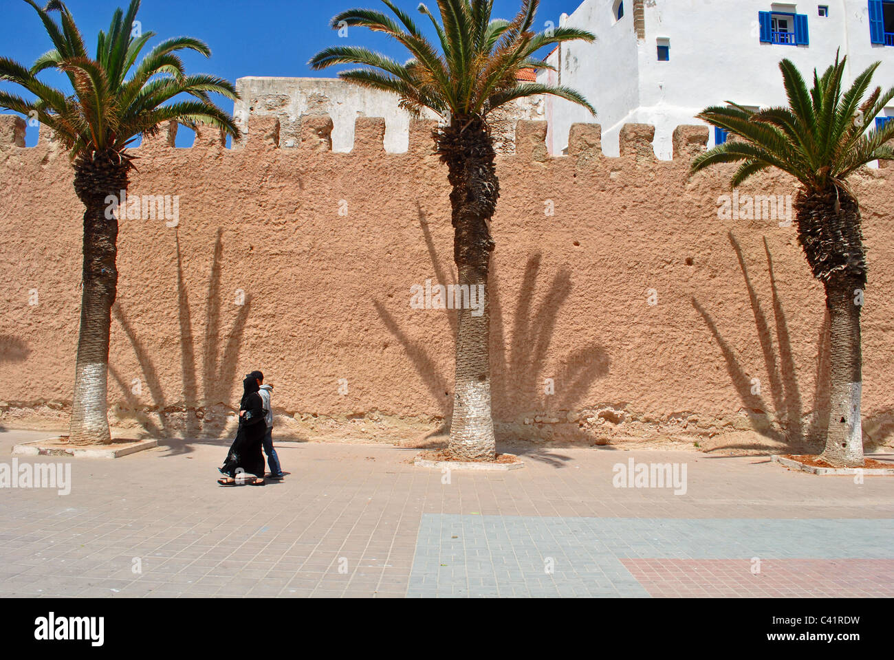 Menschen gehen vorbei an Palmen Schatten auf der Stadtmauer in Essaouira, Marokko Stockfoto