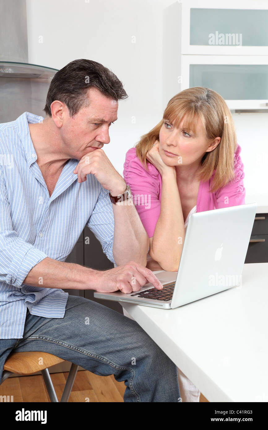 Paar auf der Suche am Laptop in Küche, besorgt oder ernsthafte Ausdrücke Stockfoto