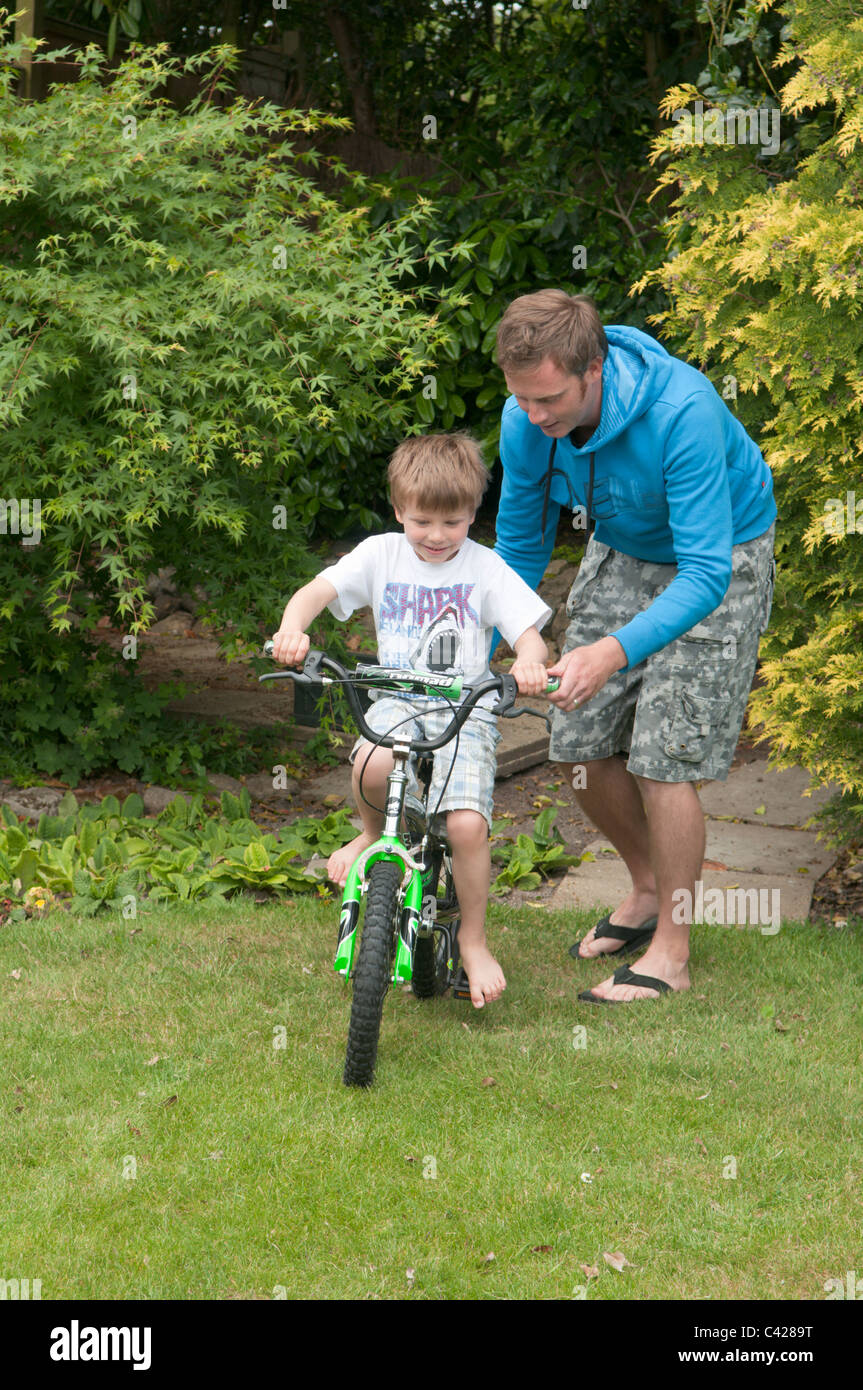 Vater im Garten hinter dem Haus seinen Sohn beizubringen, mit dem Fahrrad Stockfoto