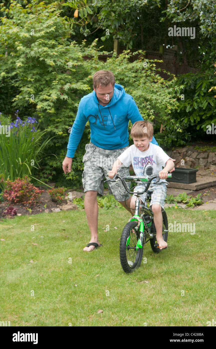 Vater im Garten hinter dem Haus seinen Sohn beizubringen, mit dem Fahrrad Stockfoto