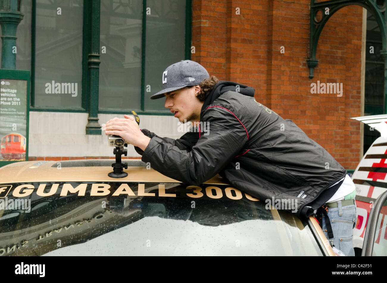 ein junger Mann, Einrichtung und Anpassung einer digitalen Aktivitäten-Action-Kamera auf einem Autodach zu Beginn der Rallye Gumball 3000. Stockfoto