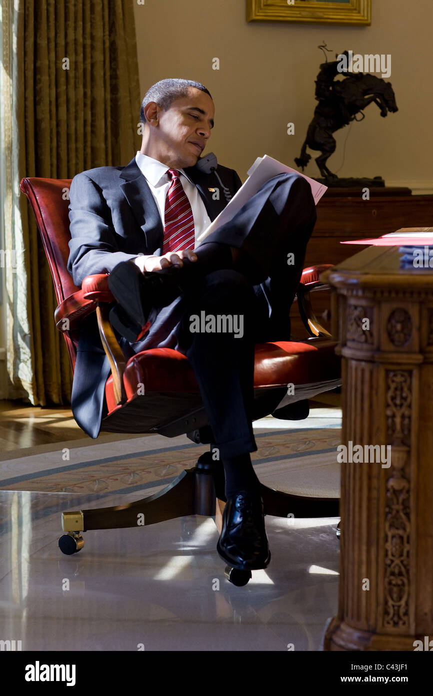Präsident Barack Obama geht über Papiere während auf dem Handy im Oval Office Stockfoto
