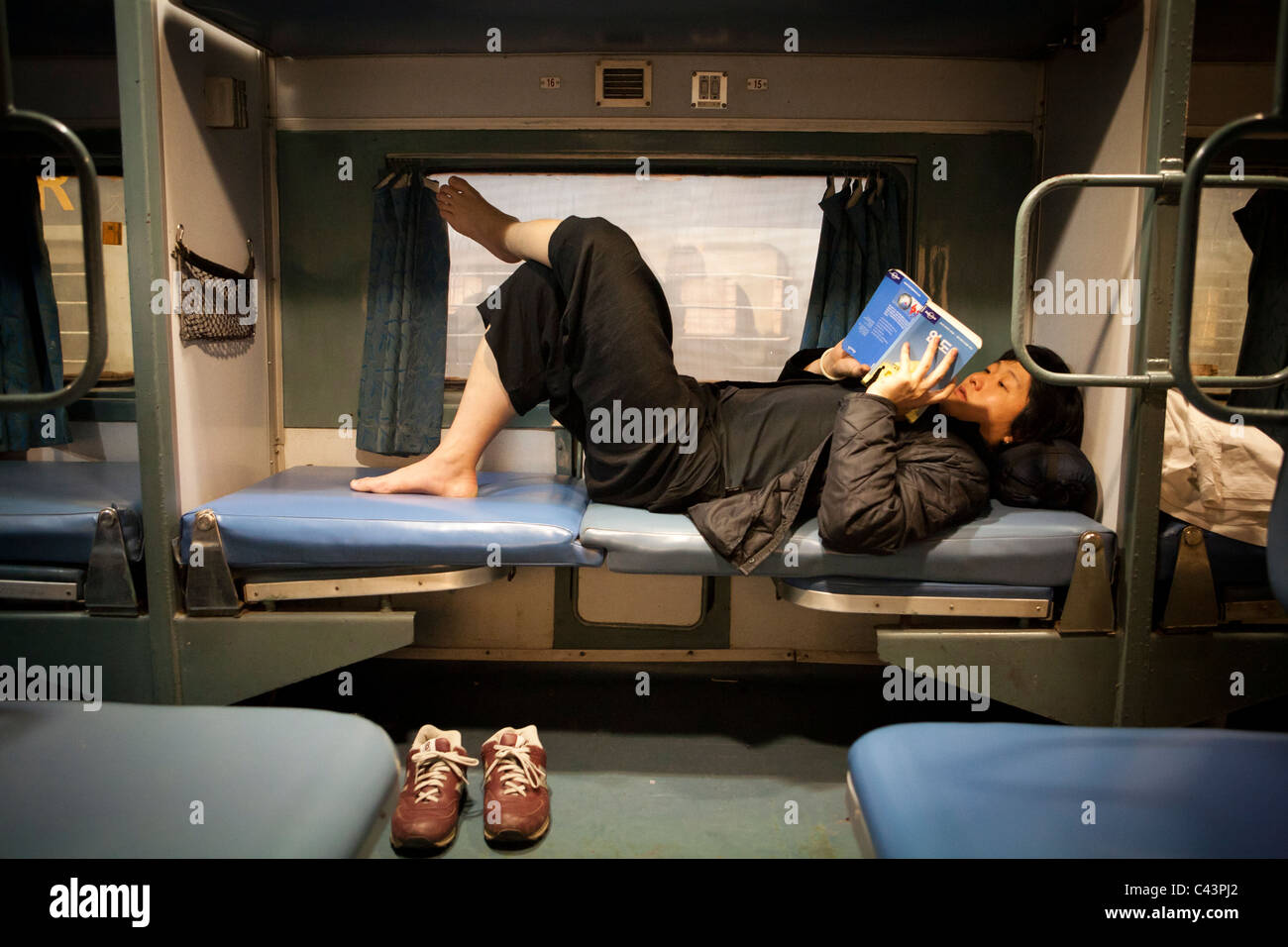 Asiatische Touristen liegen im indischen Zug nach Lesen von Lonely Planet, Punjab, Indien Stockfoto