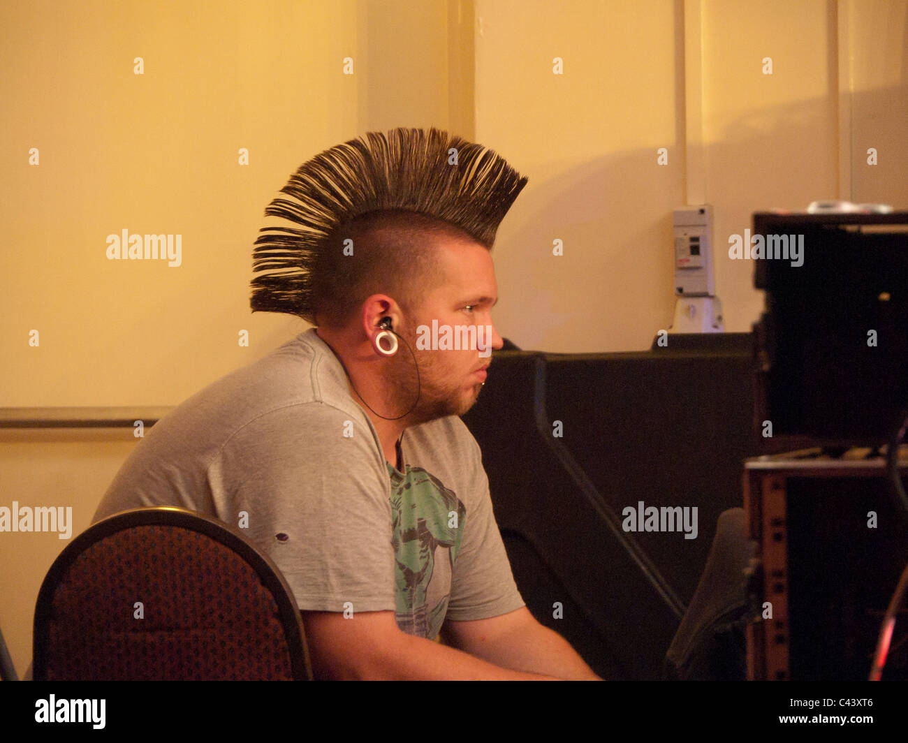 junger Mann mit Irokesenschnitt Haarschnitt und Ohrring hört Musik im club Stockfoto