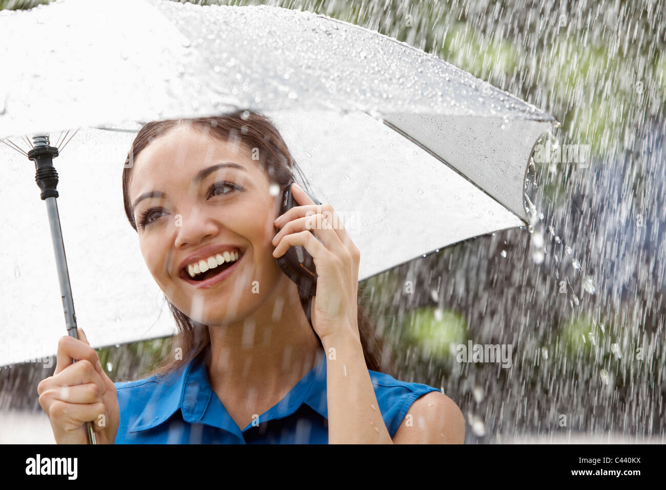 Schöne Hispanic Frau Holding Regenschirm draußen im Regen Gespräch auf ein Mobiltelefon Stockfoto