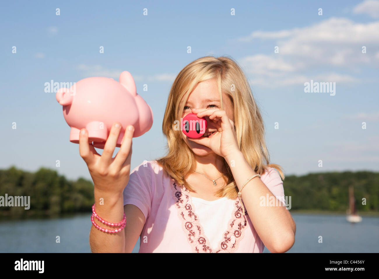 Ein junges Mädchen hält ein Schwein Nase und ein Sparschwein Stockfoto