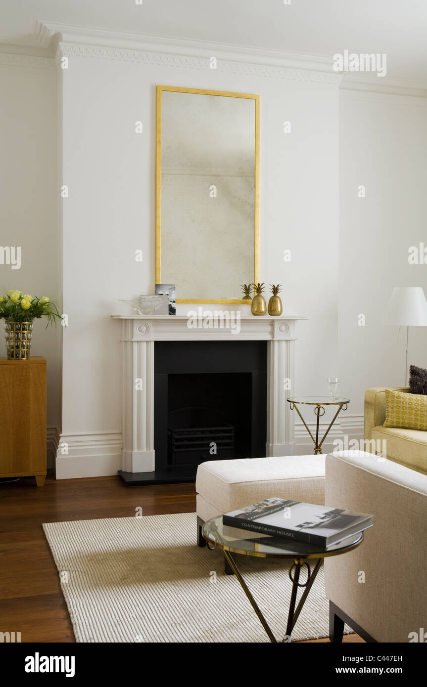 Vergoldeter Spiegel über dem Kaminsims im Wohnzimmer mit Teppich und Ottomane Stockfoto