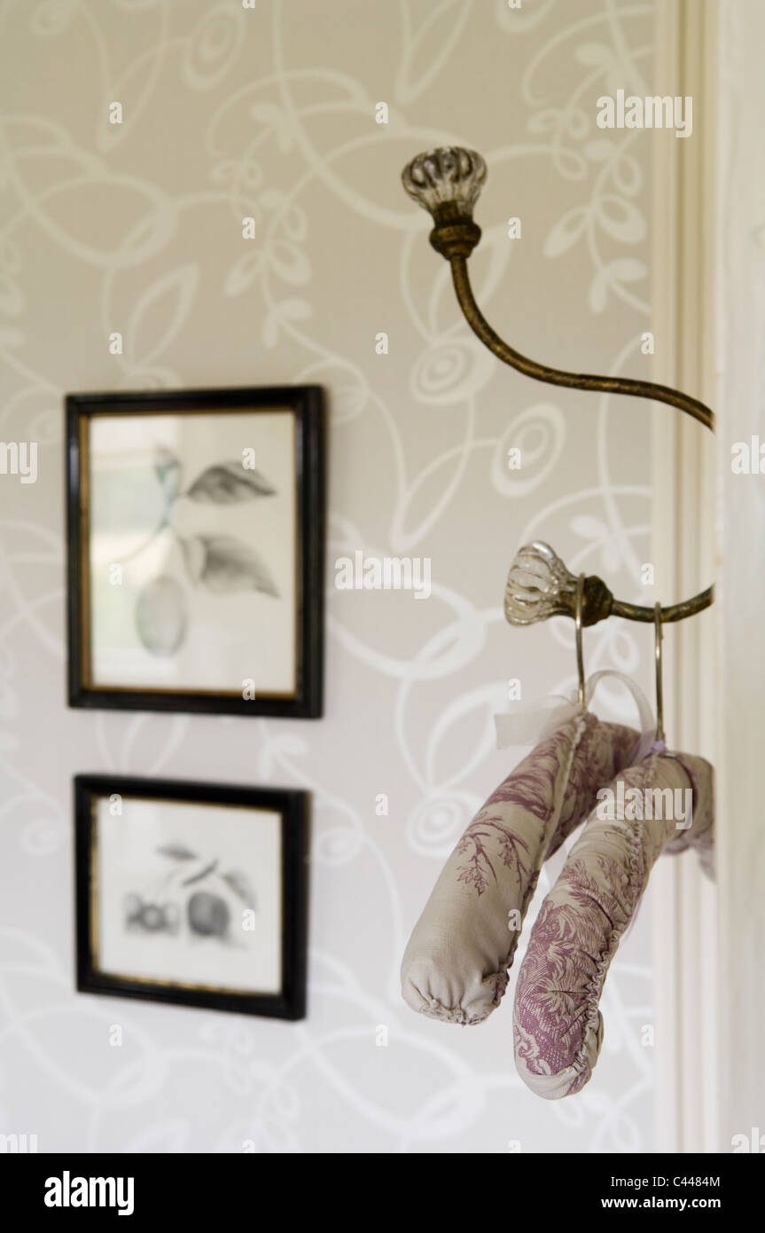 Gepolsterte Kleiderbügel an Haken auf der Rückseite einer Tür im Schlafzimmer mit gemusterten Tapeten Stockfoto