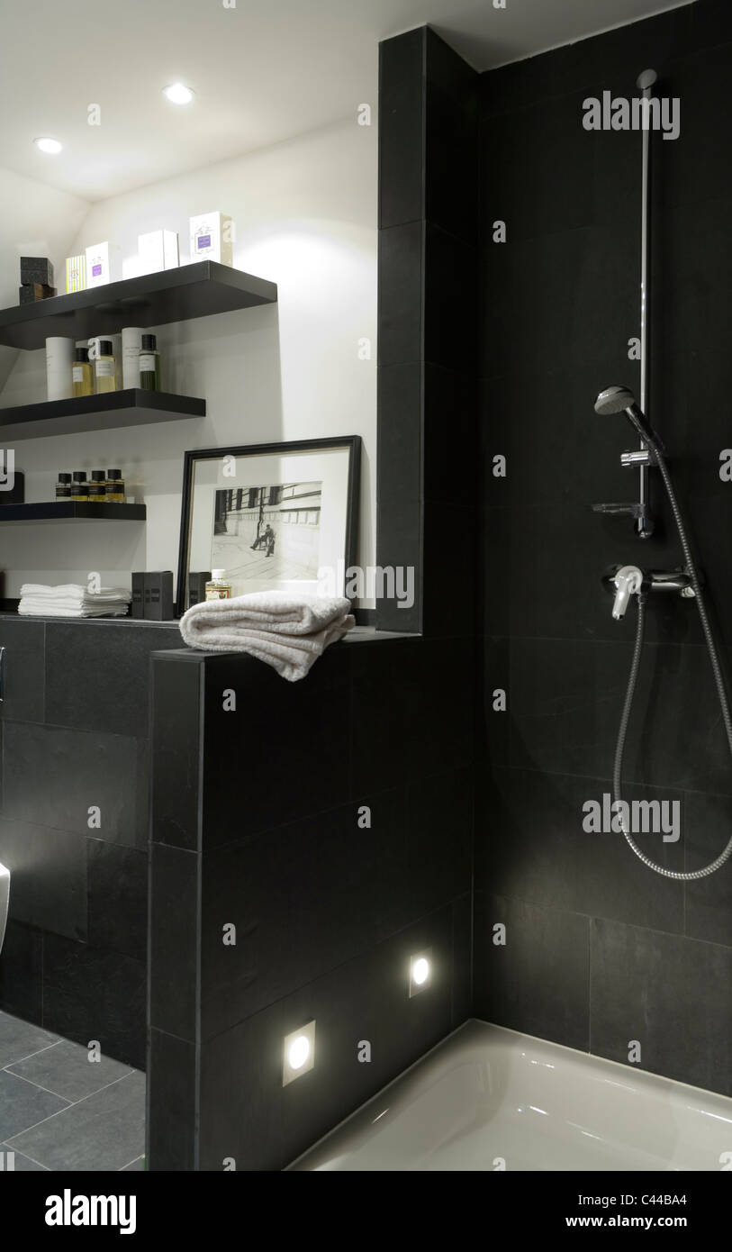Modernes Bad mit schwarzen Duscheinheit, Regale und Kunstwerke. Stockfoto