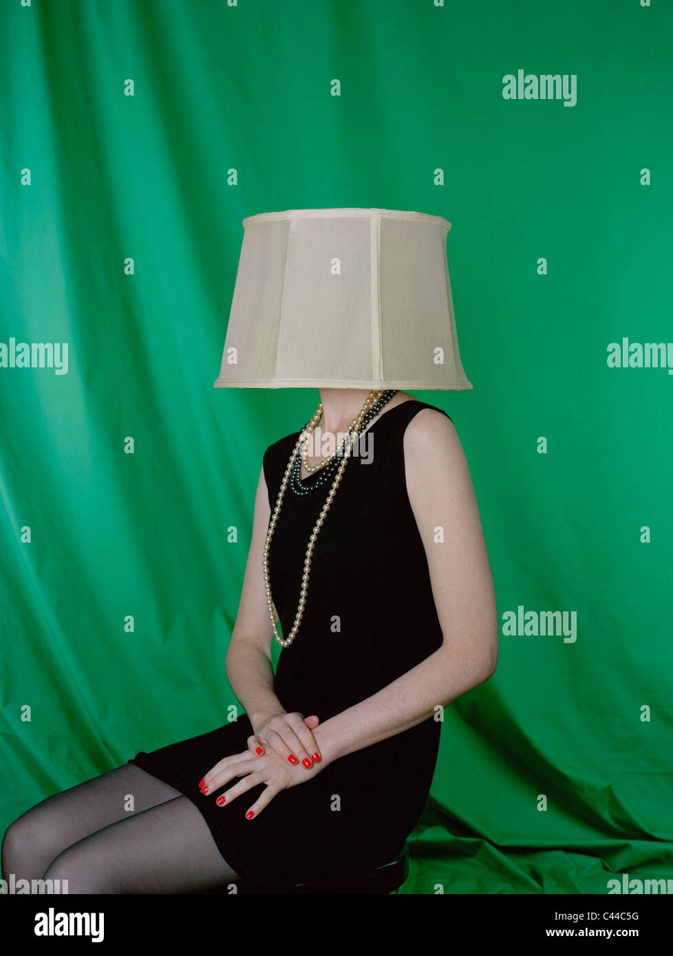 Eine gut gekleidete Frau trägt einen Lampenschirm auf den Kopf Stockfoto