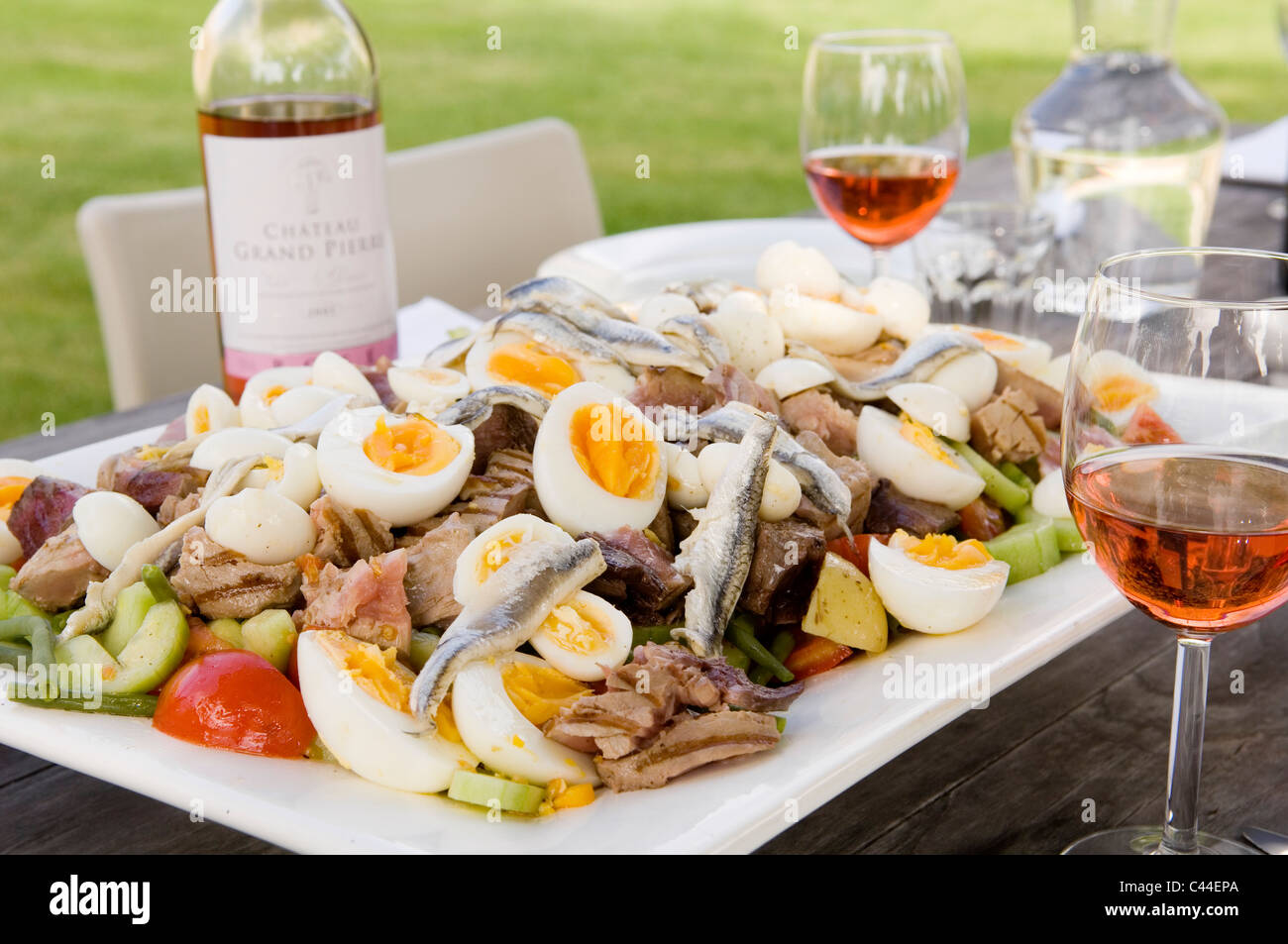 Große Platte mit Salat Nicoise mit Thunfisch, Sardellen und Eiern auf Gartentisch mit Roséwein Stockfoto