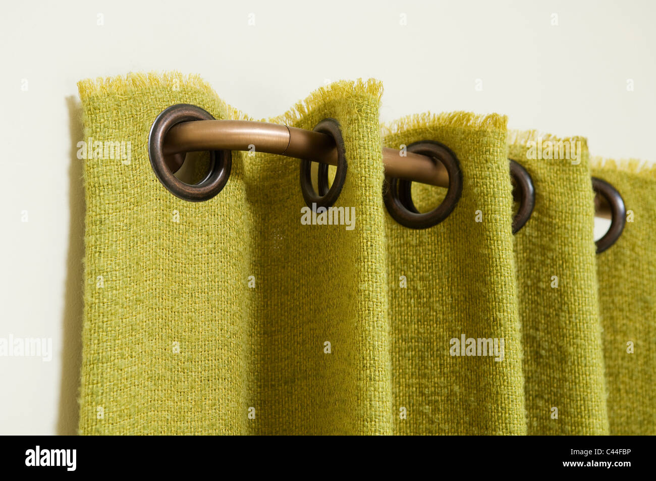 Detail von einem grünen Vorhang mit Ösen, angeschlossen an eine gebogene Messing-Vorhangstange Stockfoto