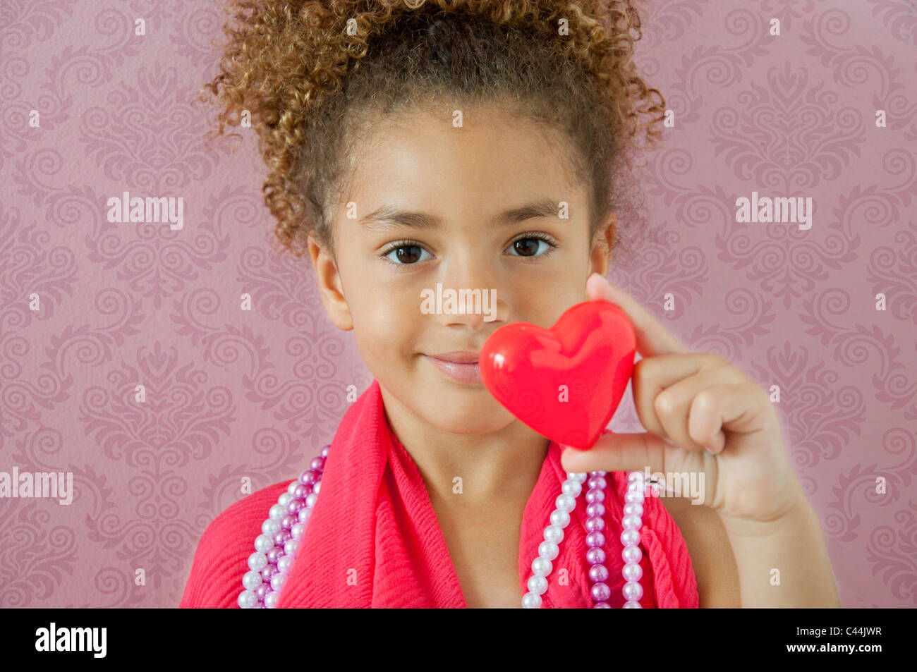 junges Mädchen hält ein Herz in einem rosa Zimmer Stockfoto