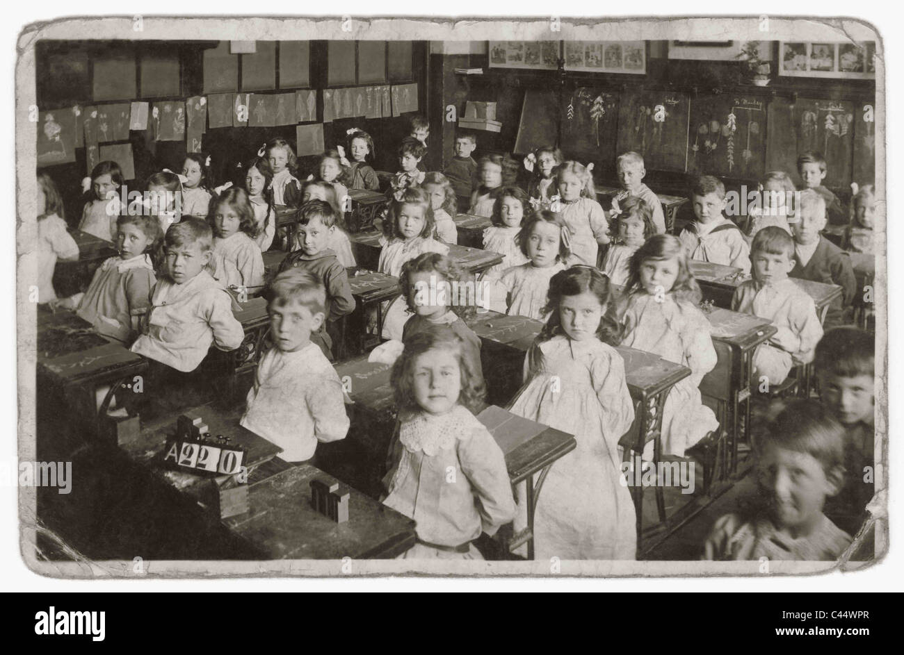 Formale Porträt des Edwardianischen und viktorianischen Säuglinge an Ihrem Schreibtisch in einem strengen Grundschule Klassenzimmer sitzen während einer Lektion mit Kreide auf Schiefer. ca. 1908, U.K. Edwardians, Victorians Stockfoto