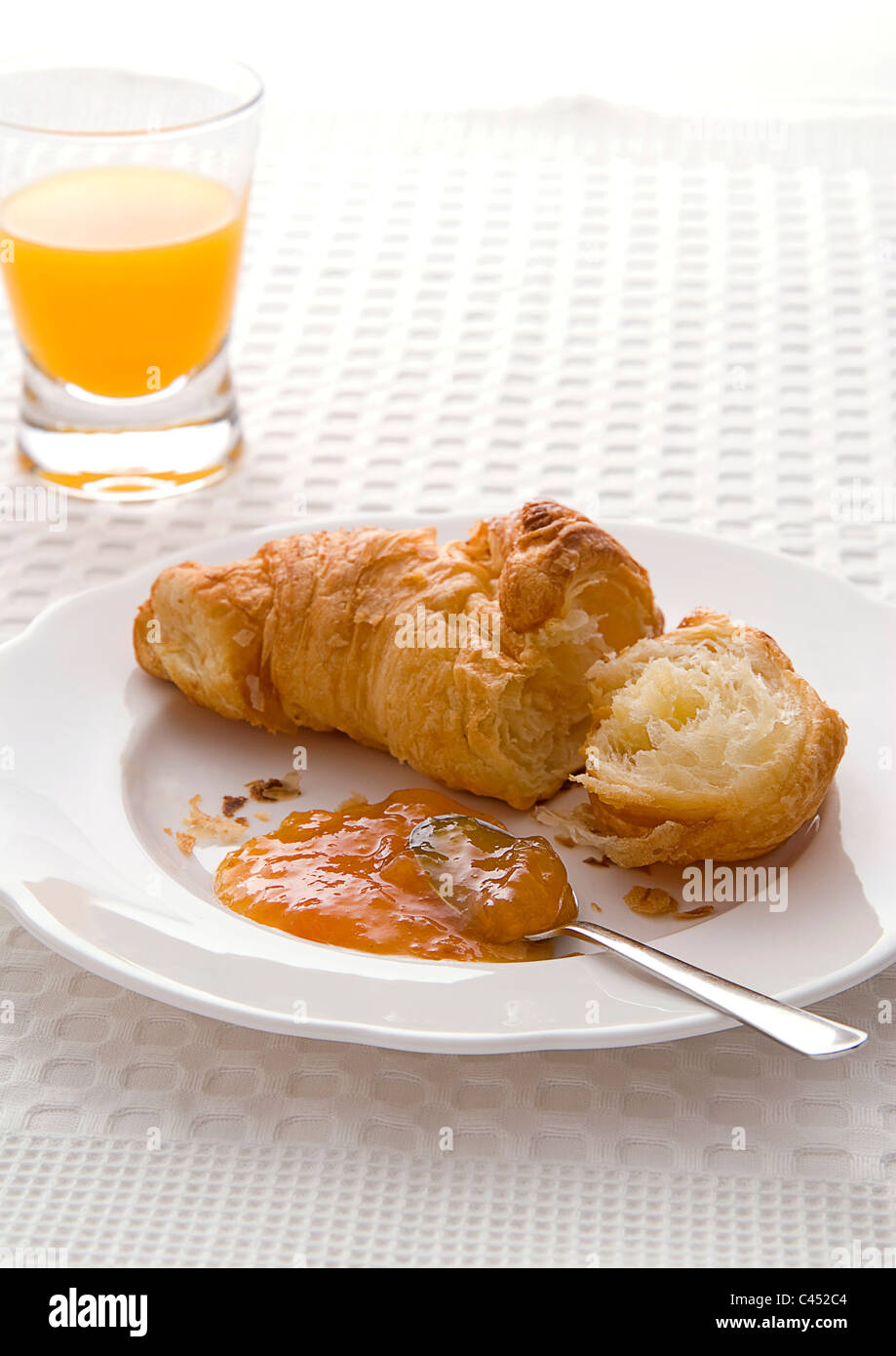 Croissant mit Marillenmarmelade und Glas Fruchtsaft, Nahaufnahme Stockfoto
