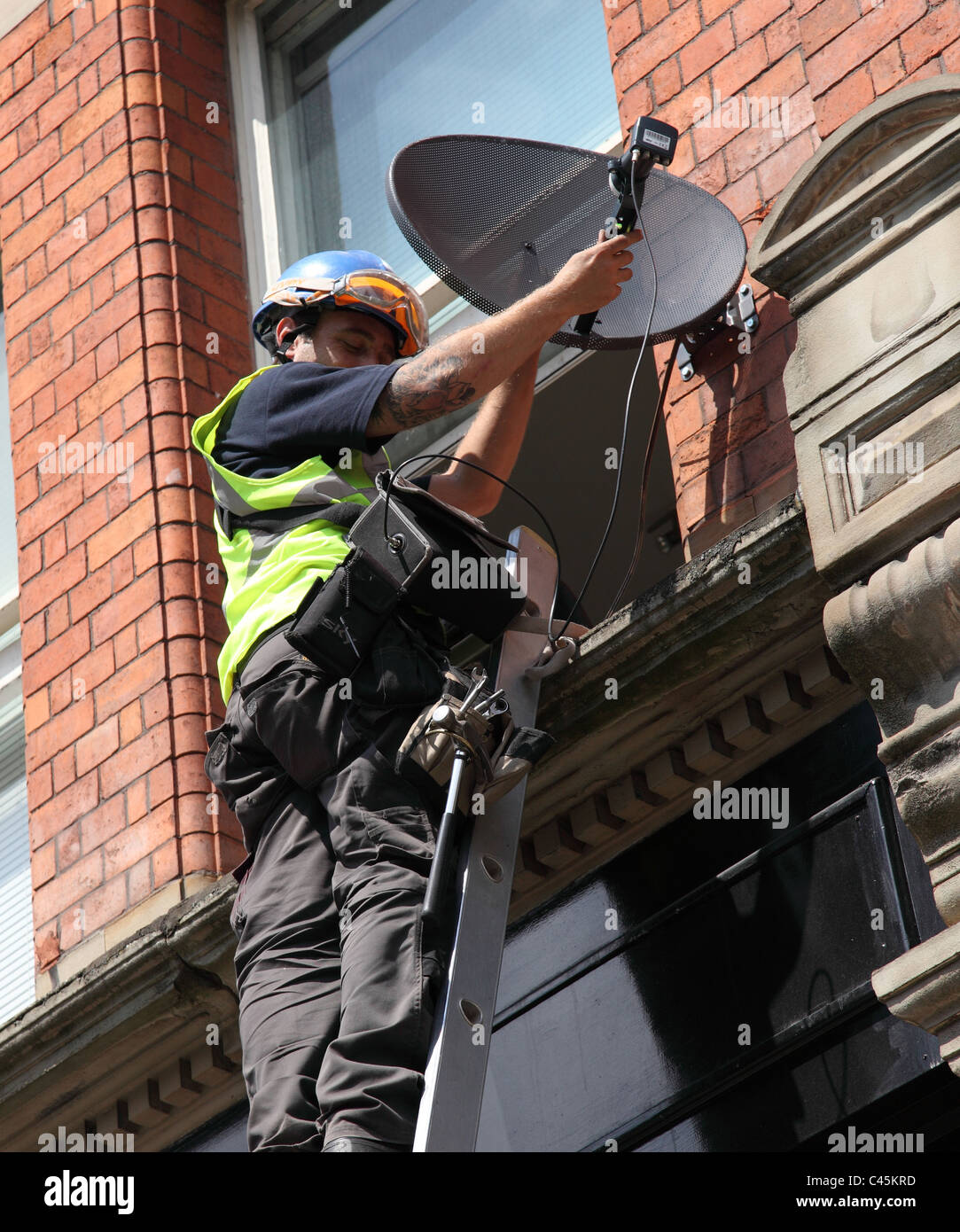 Ein Ingenieur, der Installation einer Satellitenschüssel zu einem Gebäude in Großbritannien. Stockfoto
