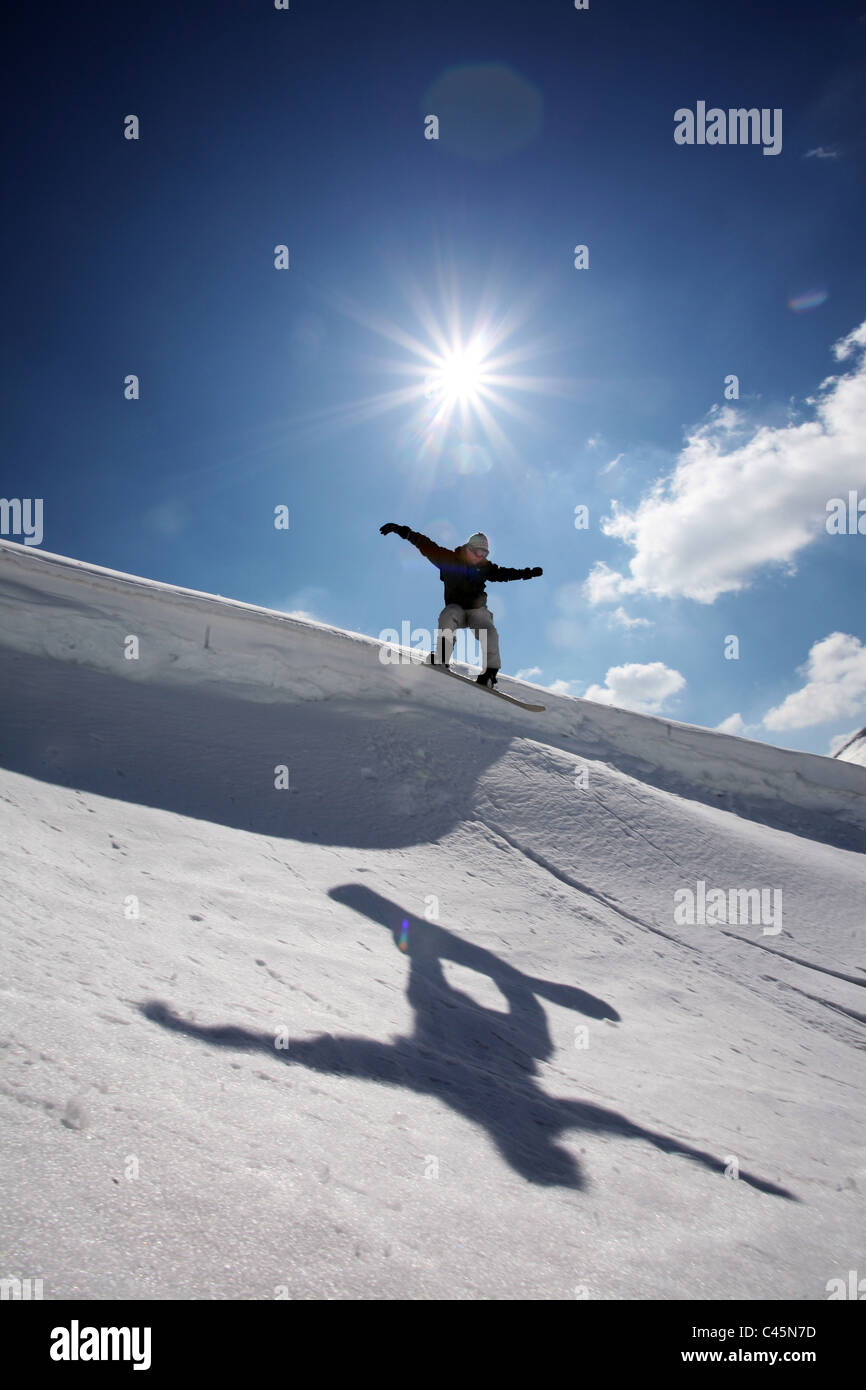 Ein Snowboarder springt über ein Gesims in La Thuile, ein Ski-Resort in Italien, seine Schatten im Schnee unter der Sonne starburst Stockfoto