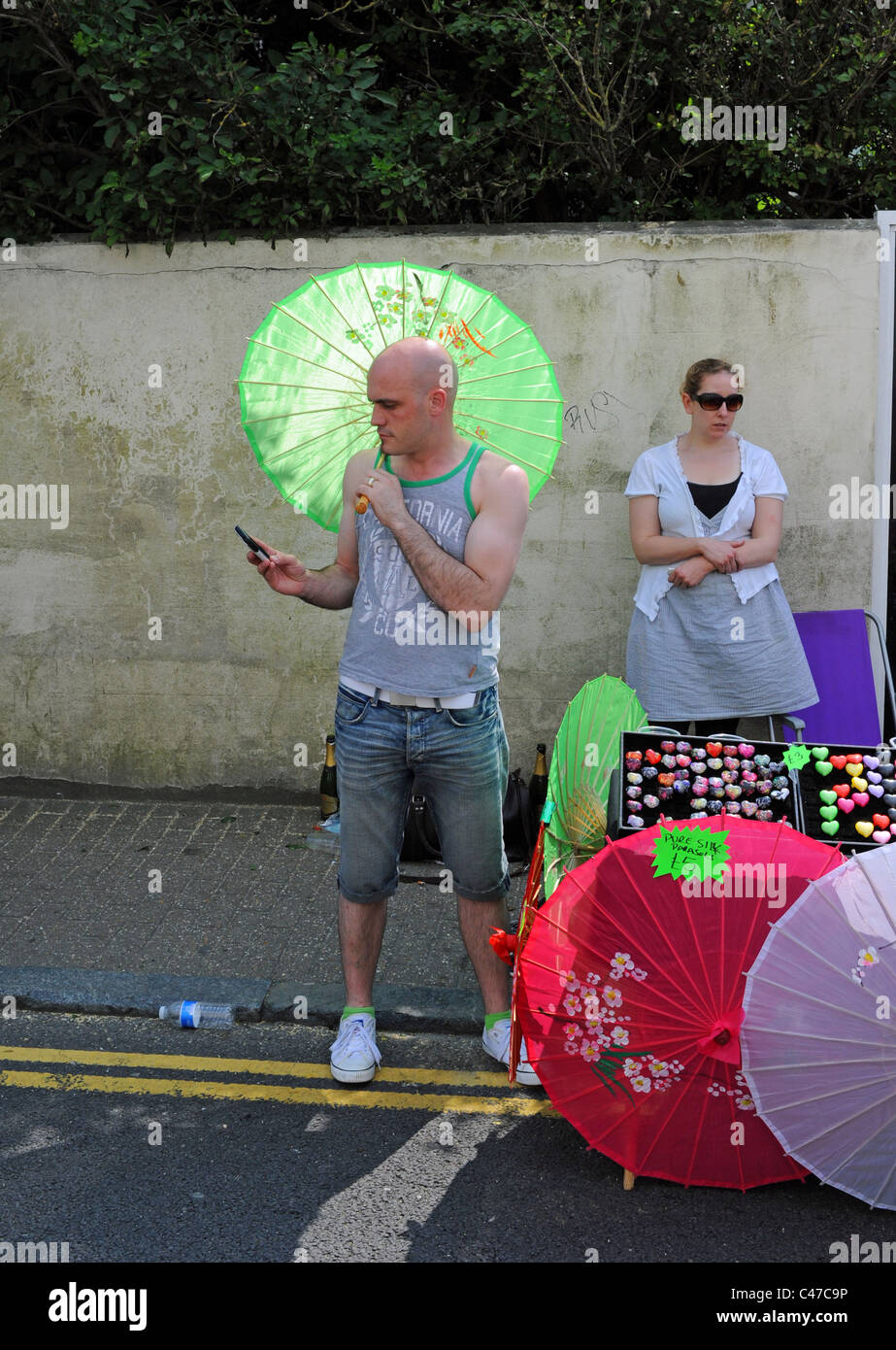 Mann mit Handy halten grün Sonnenschirm am Stand in Kemptown Karneval Brighton UK Stockfoto