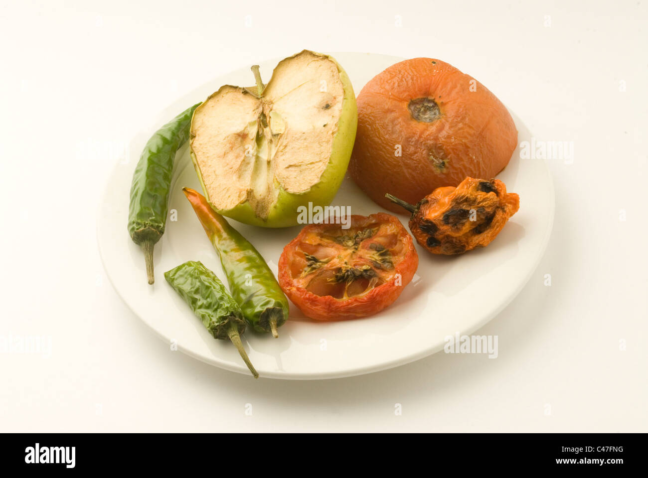 Alten faulen Apfel, Chilis und Tomaten auf einem Teller. Sie hatten im Kühlschrank für etwa einen Monat bis zum Zerfall gelassen worden. Stockfoto
