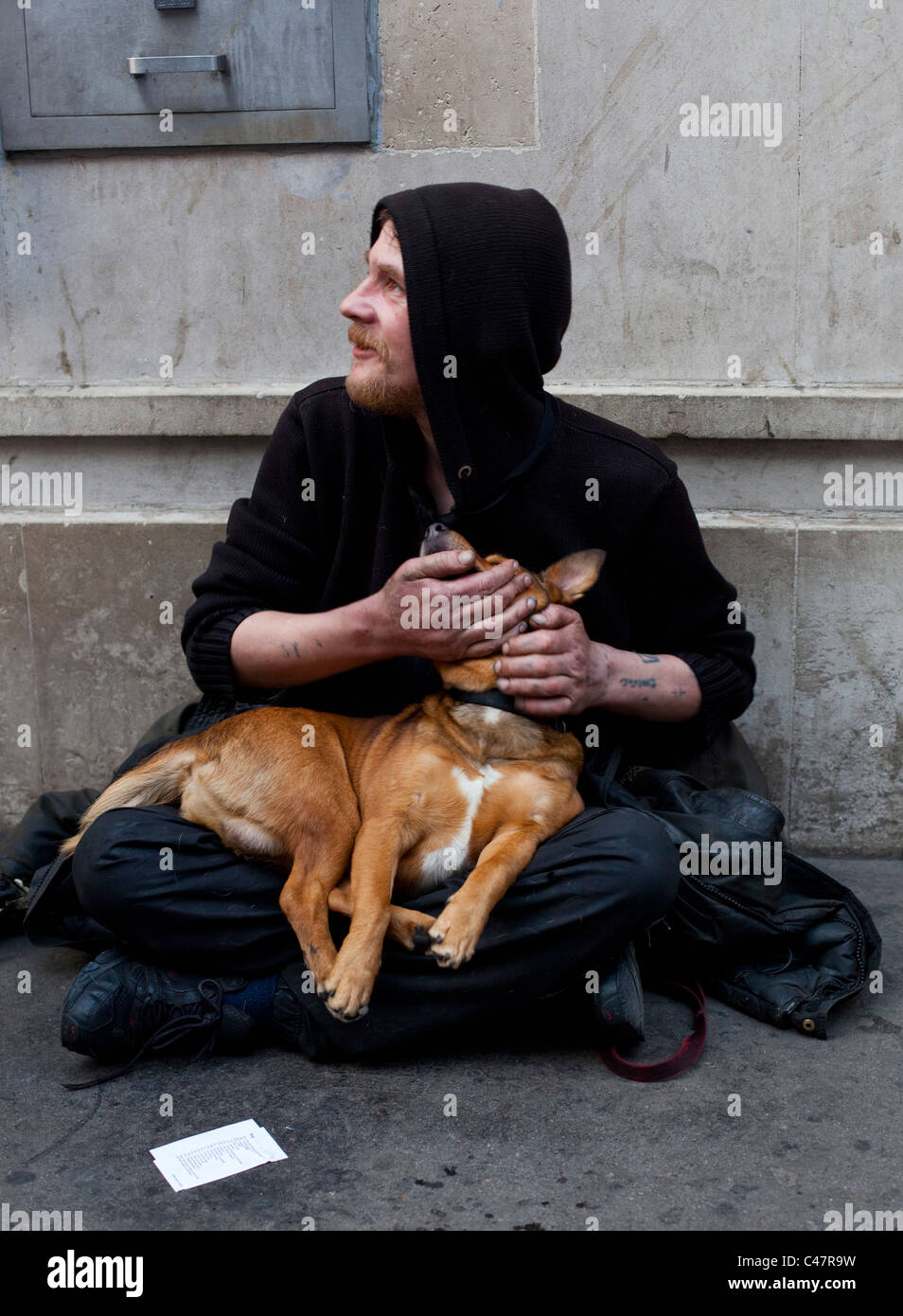 Ein obdachloser Mann um Geld betteln auf dem Bürgersteig und seinem Haustier Hund halten, London, England, UK. Stockfoto