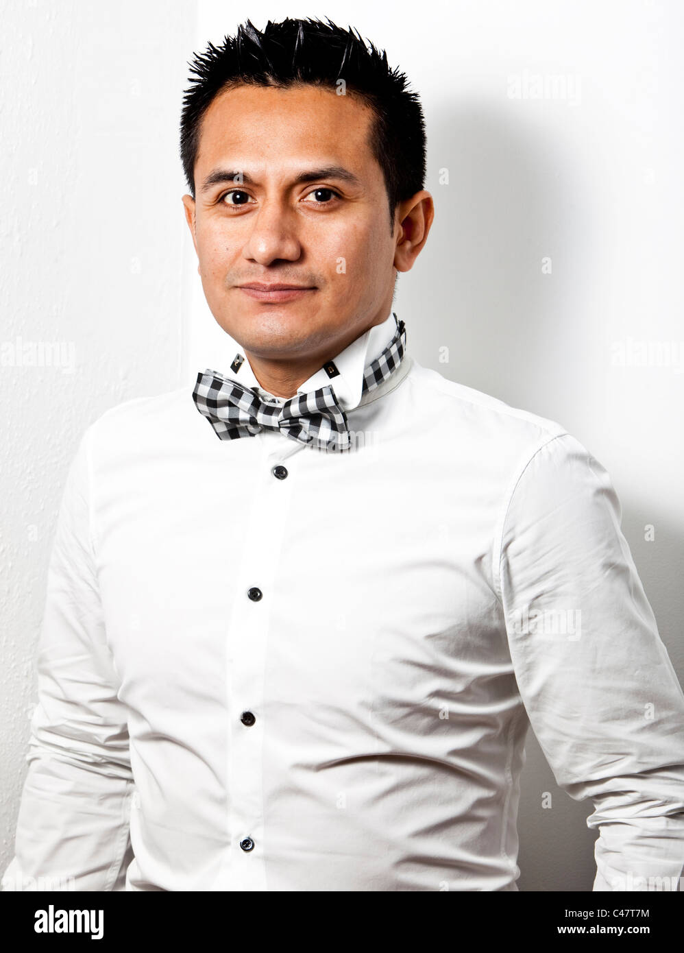 Halblängen Porträt eines lateinischen trägt weißes Hemd und eine Fliege vor weißem Hintergrund, London, England, UK Stockfoto