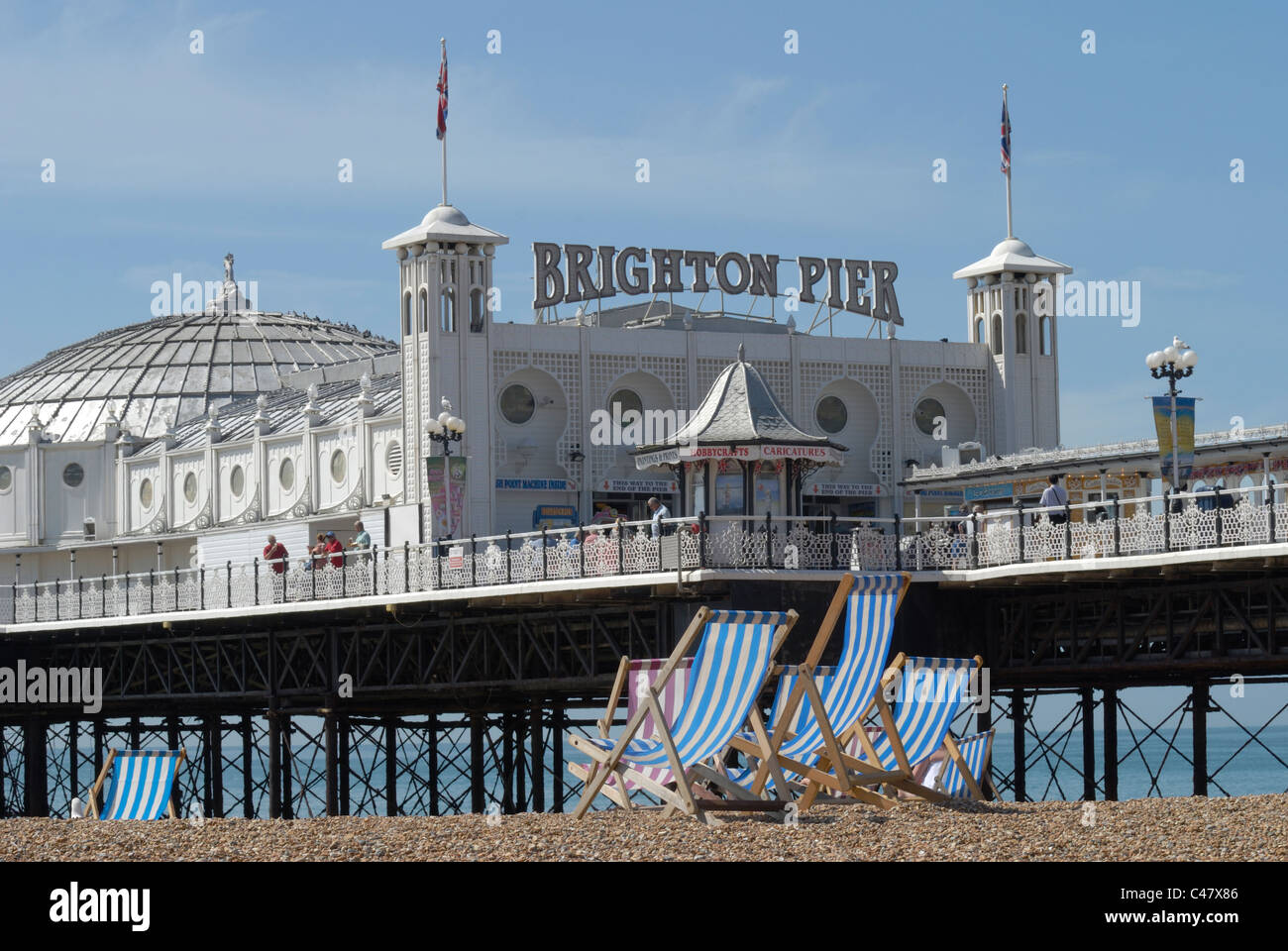 Liegestühle auf den Schindel von Brighton Beach mit Pier im Hintergrund. East Sussex. England Stockfoto