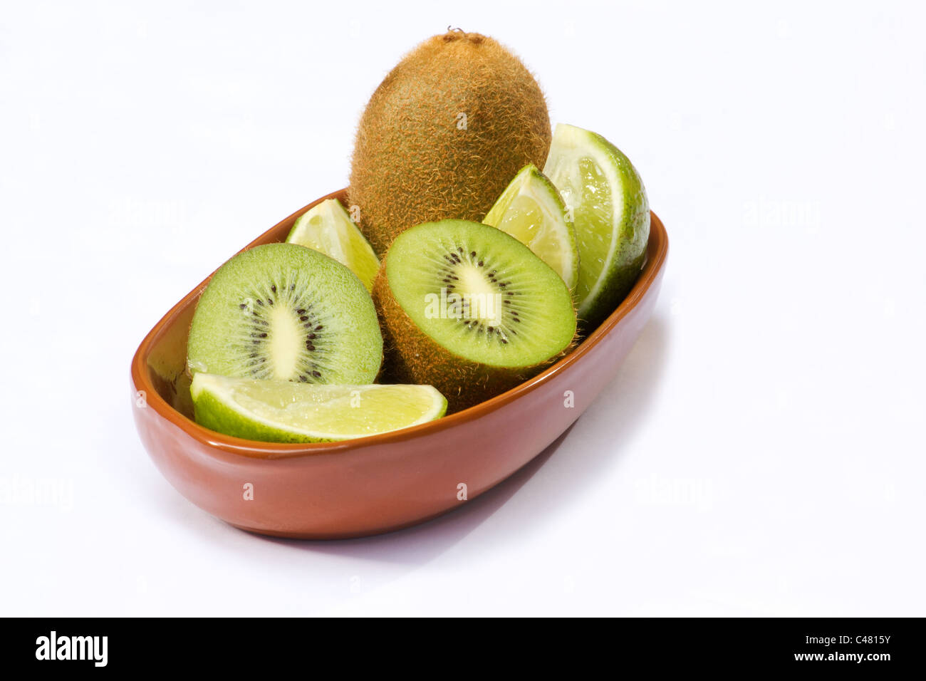 Nahaufnahme von Kiwi und Limette Vierteln in Terrakotta Schale auf weißem Hintergrund Stockfoto