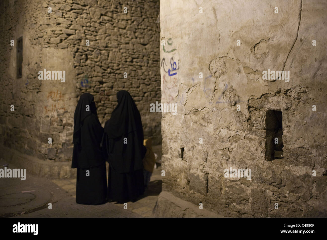 Zwei Frauen tragen traditionelle schwarze Abaya (Hijab) sprechen in der Nacht in der alten Stadt von Sana'a, Jemen. Stockfoto
