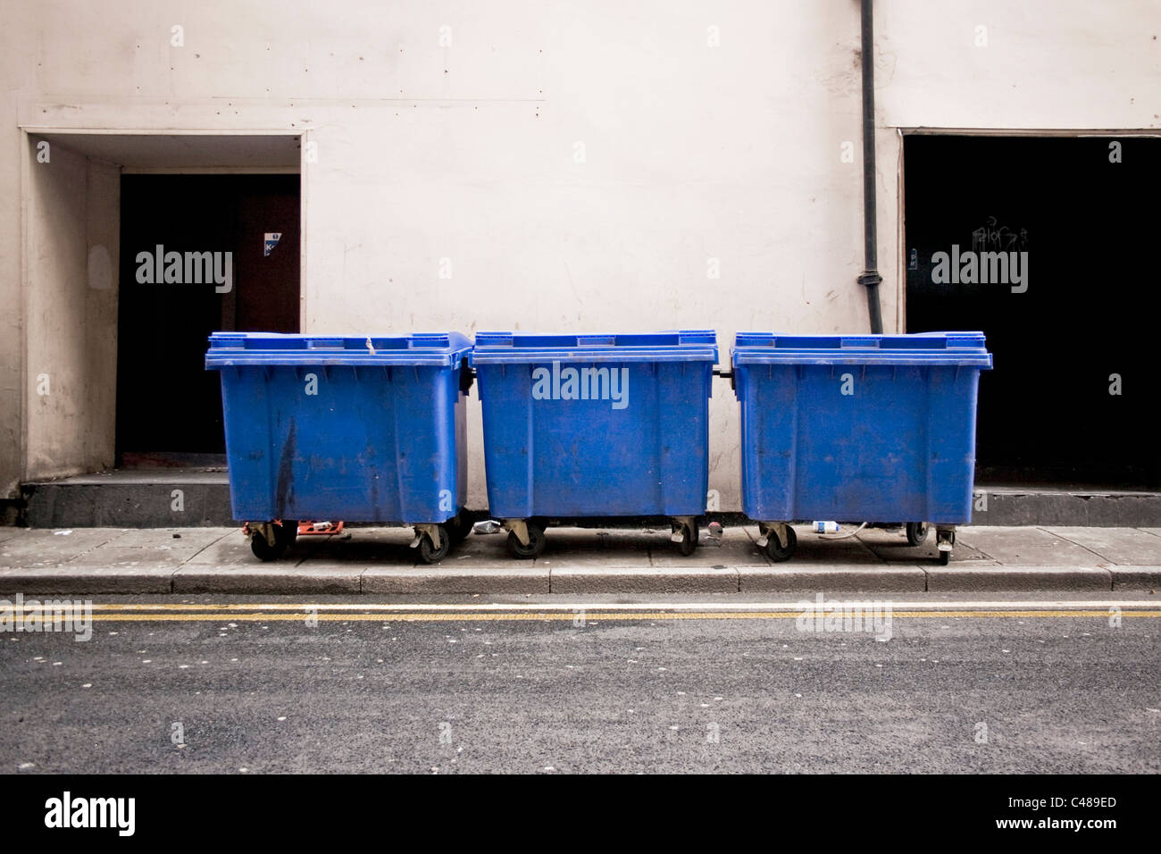 Drei große Mülltonnen stehen an der Seite von einer leeren Manchester Straße. Stockfoto