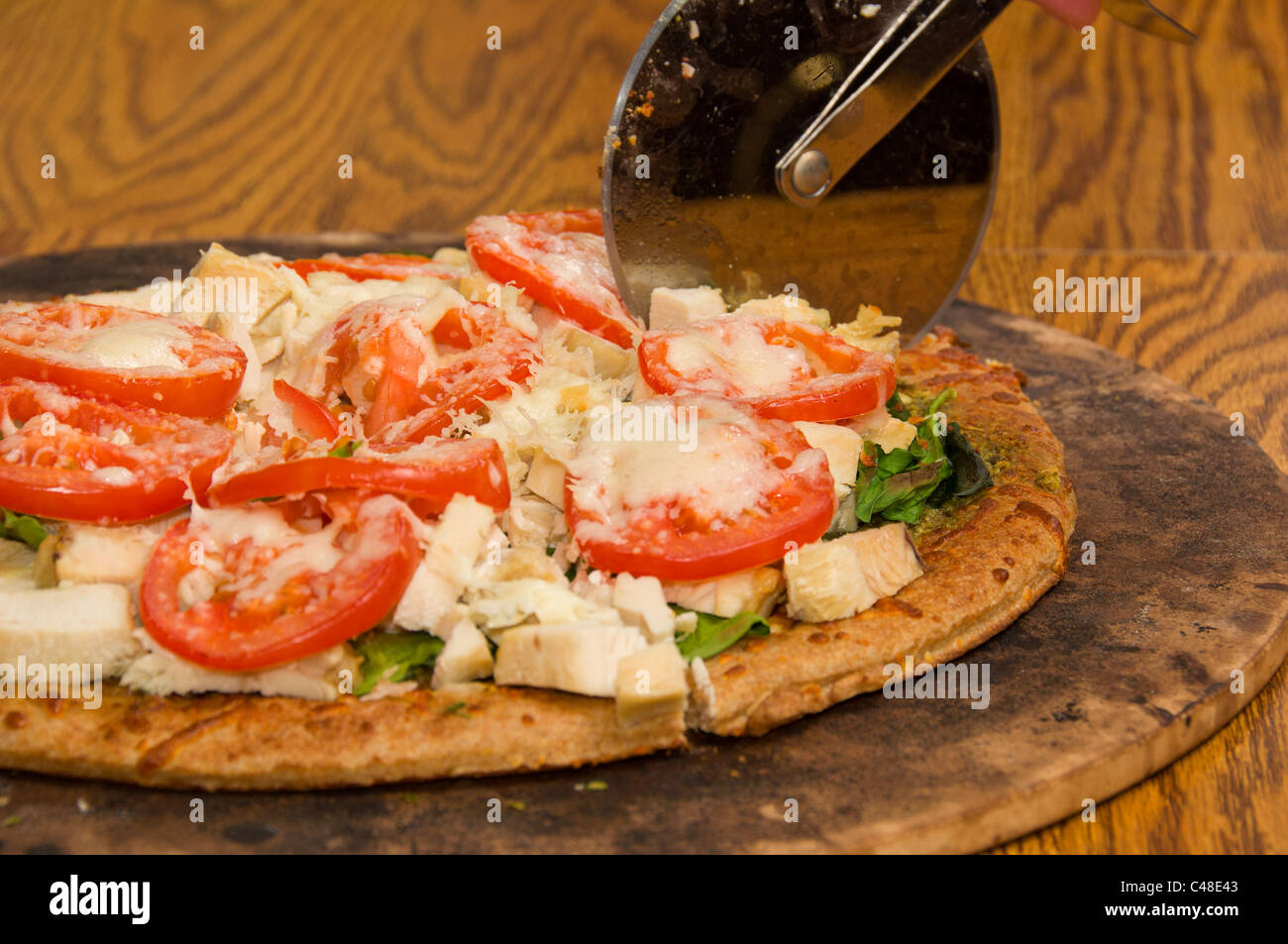 Eine Pizza mit Tomaten, Spinat, gedünstetes Huhn, Pesto, Mozzarella und Hand Made Kruste mit einem Pizzaschneider gemacht Stockfoto